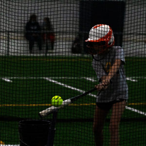 Girl holding a softball bat trying to hit the softball