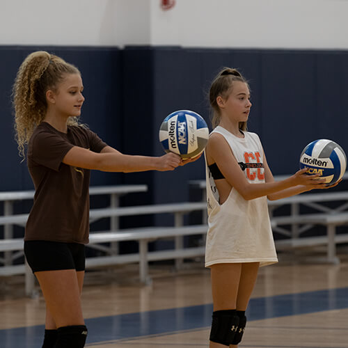 Two girls holding volleyballs